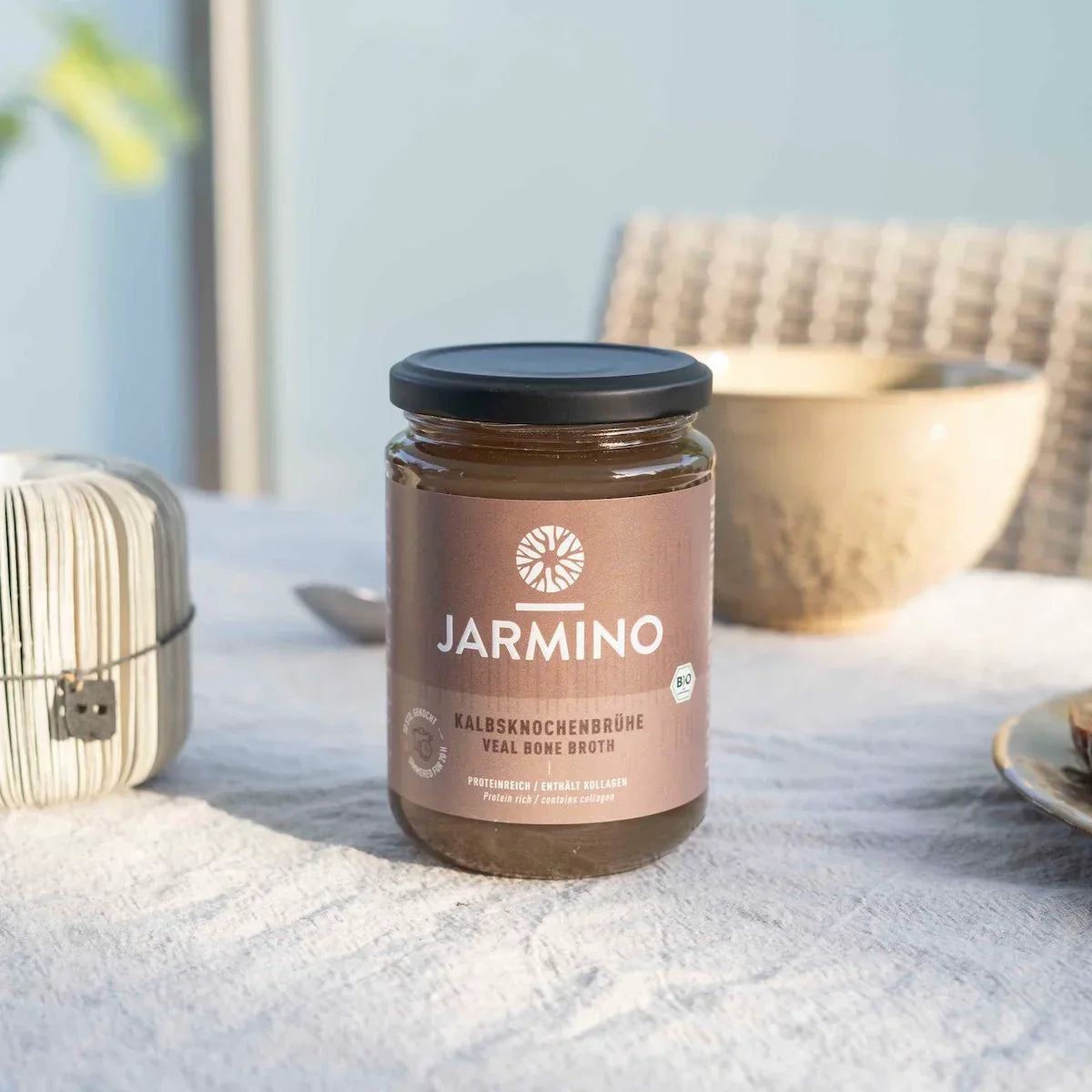 Jarmino Kalbsknochenbrühe 350ml – Glasflasche auf Sand, dekorativ arrangiert, natürliche Atmosphäre